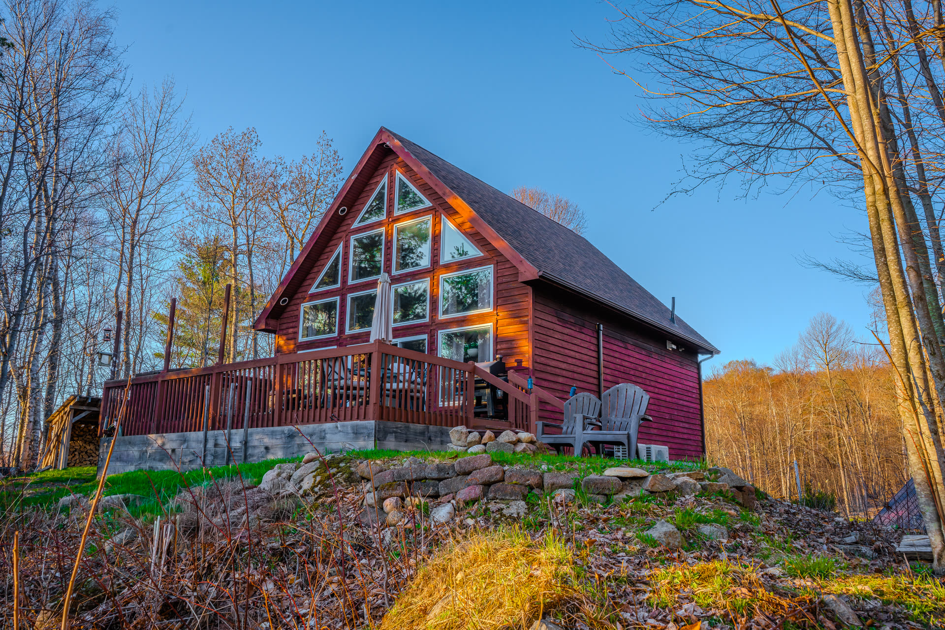A-frame red cedar cabin at golden hour with tall windows and Adirondack chairs